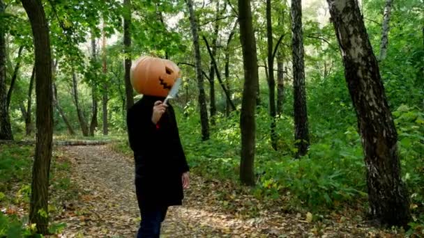 Halloween. A crazy and cheerful man with a pumpkin on a walk with a knife in the autumn forest. - Footage, Video
