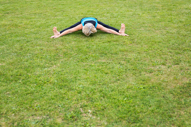 Uma mulher de meia-idade praticando ioga descalça lá fora em um parque gramado
 - Foto, Imagem