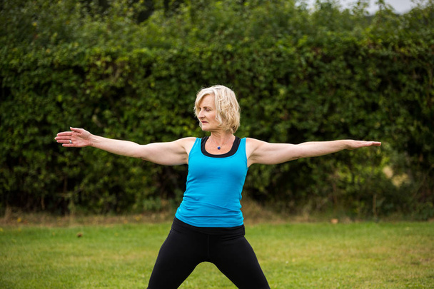 Kobieta w średnim wieku uprawiająca jogę boso na zewnątrz w trawiastym parku - Zdjęcie, obraz