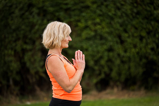 Une femme d'âge moyen pratiquant le yoga pieds nus à l'extérieur dans un parc herbeux
 - Photo, image
