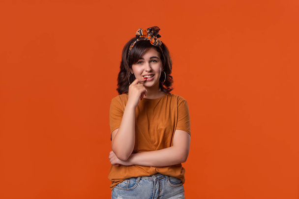 Smiling brunette woman in a t-shirt and beautiful headband standing isolated over orange background. Place for ad. - Fotó, kép