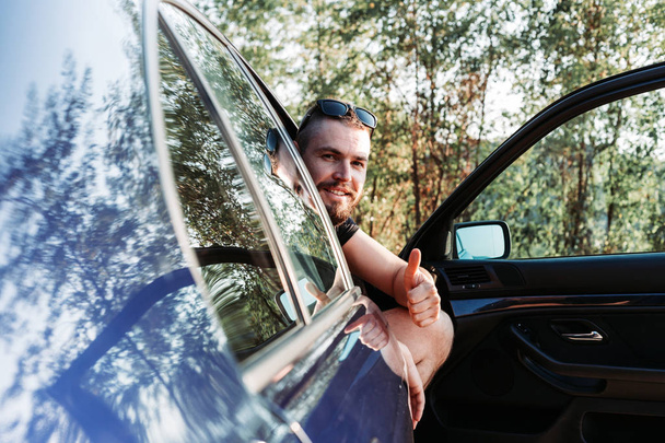 Aranyos, szakállas férfi ül az autó elején, nyitott ajtó - Fotó, kép