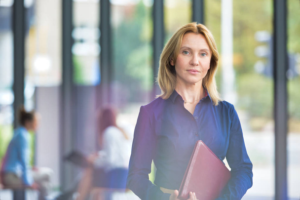 Confident businesswoman holding document while standing against colleagues in office meeting - Photo, Image