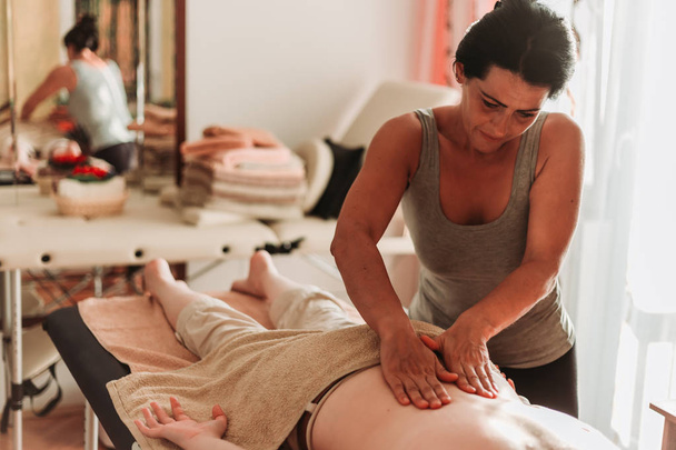 Close-up photo of masseuse massaging her client back. Red spa light. - Фото, изображение