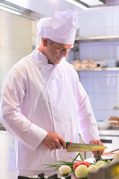 Portrait of confident mature chef cutting vegetables in kitchen - Foto, imagen