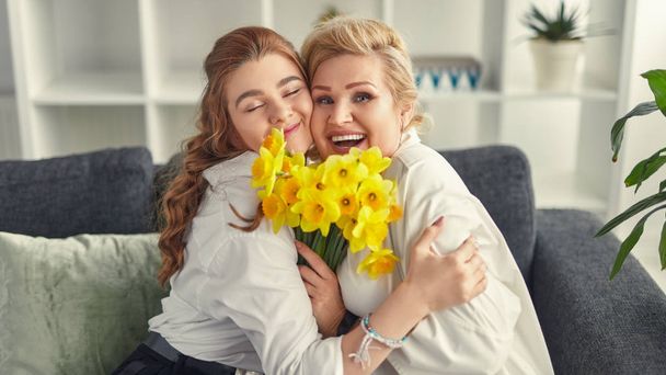 Laughing grandmother and granddaughter cuddling and holding flowers - Фото, зображення