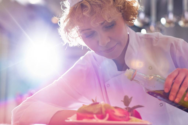 Усміхнений зрілий шеф-кухар поливає олію на салат у тарілці в ресторані
 - Фото, зображення
