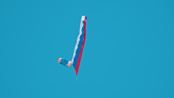 Muž plující na obloze jasně modrý s otevřeným padákem a ruskou vlajkou. - Záběry, video