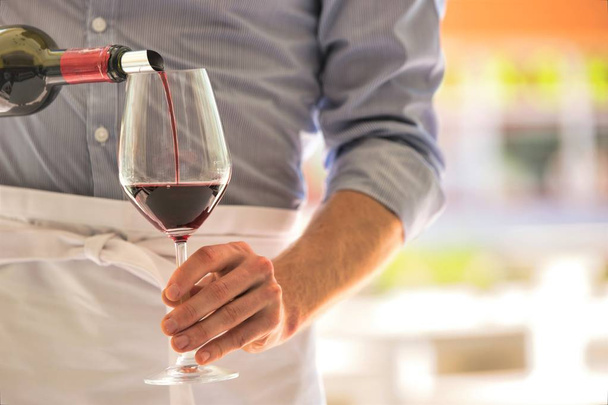 Midsection of waiter pouring red wine in wineglass at restaurant - Foto, imagen