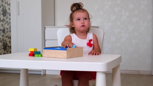 little bored girl, 2 years old, plays educational toys, stacks and arranges colorful figures. Learning through experience concepts, rough and fine motor skills - Metraje, vídeo