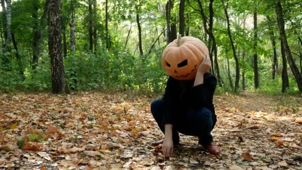 秋の森の地面に座っている悲しいカボチャ頭の男。ハロウィーンコンセプト.4k - 映像、動画