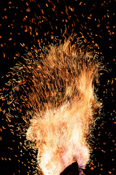 Llama de fuego con chispas rojas ardientes volando sobre un fondo negro. Ardientes partículas naranjas brillando volando en el cielo nocturno. Primer plano de hermosa llama
 - Foto, Imagen