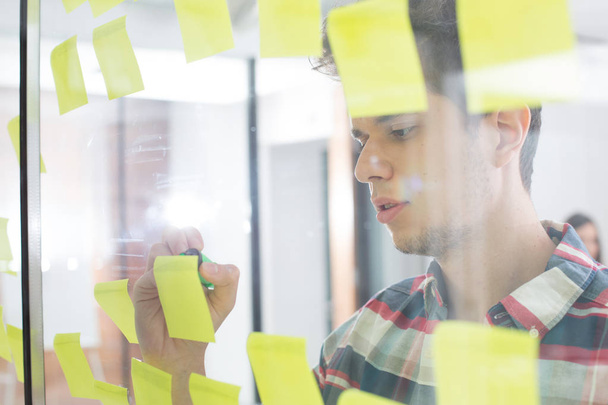 Young businessman writing on sticky notes in office - Photo, image