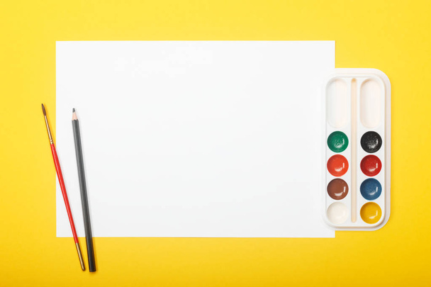 Blank paper with pencil, brush and paints on yellow background. Artist workplace concept with copy space for your ideas. - Foto, Imagen