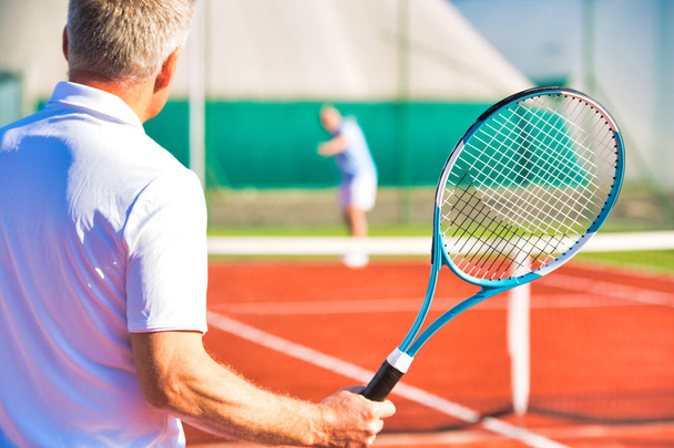 Active seniors playing tennis on sunny day at red court - Fotografie, Obrázek