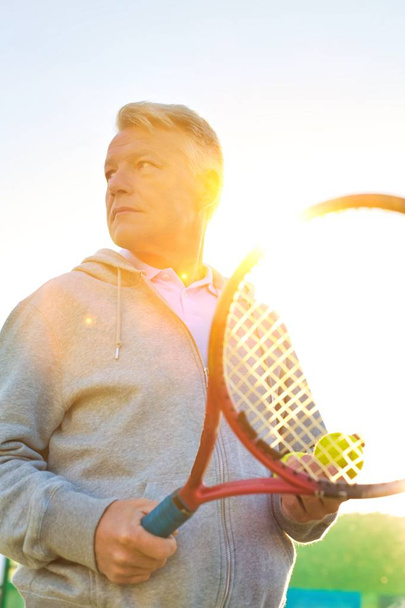 Dojrzały mężczyzna trzyma piłki tenisowe i rakiety w letni dzień - Zdjęcie, obraz