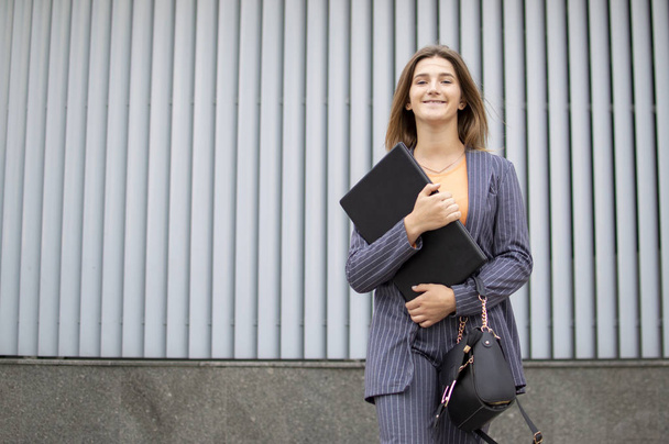 femme d'affaires avec ordinateur portable séjour dans la ville sur le fond du mur, une fille en costume rayé en utilisant l'ordinateur à l'extérieur
 - Photo, image