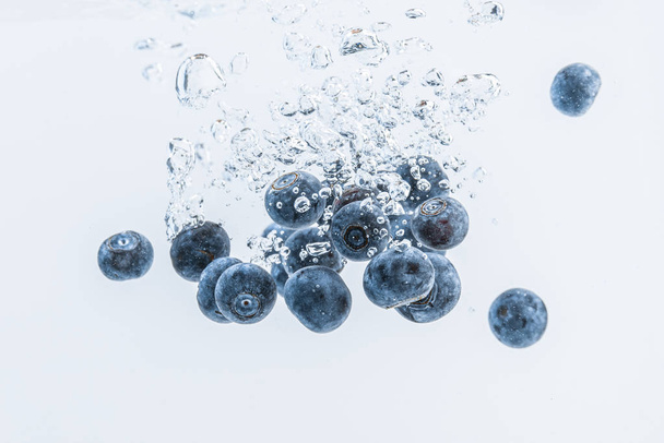 Fresh blueberries falling in water on white background. Fruits splashing into clear water. - Foto, Imagen