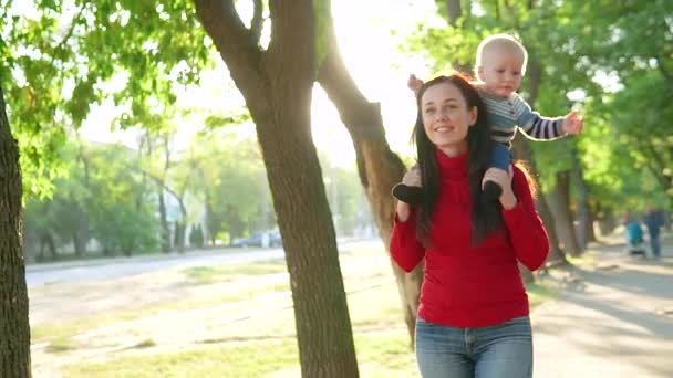 Nuori äiti ja hänen poikansa hymyilevät ja kävelevät puistossa. Poika istuu tytön selässä punaisessa puserossa.
 - Materiaali, video