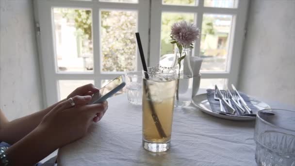 A young girl uses a smartphone in a cafe, next to her elderberry soda. - Séquence, vidéo