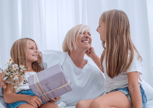 happy mom with flowers and gifts sitting with her daughters on the bed. - Foto, Bild