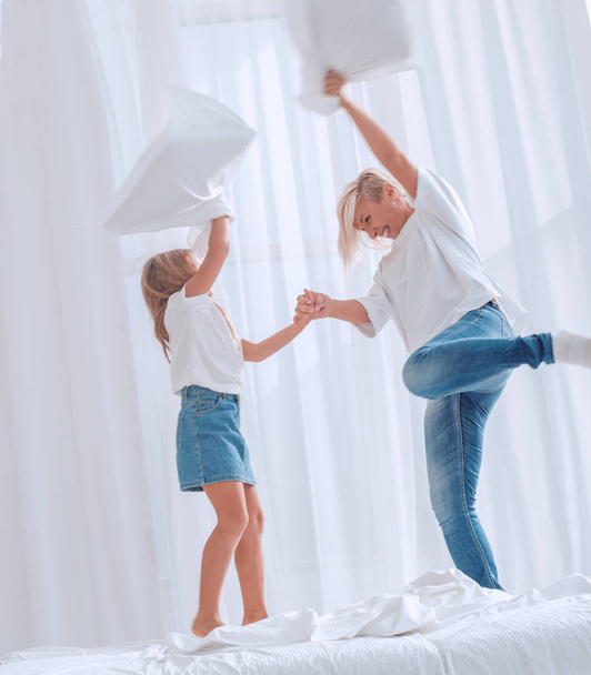 close up. mom and daughter have a pillow fight on the bed - Foto, afbeelding