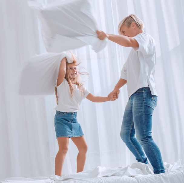 close up. mom and daughter have a pillow fight on the bed - Photo, Image