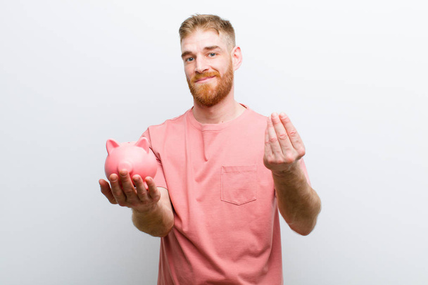 young red head man holding a piggy bank against white background - Photo, image