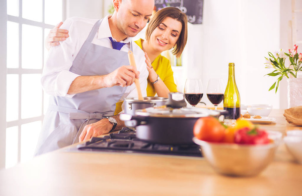 Attractive couple in love cooking and opens the wine in the kitchen while they cook dinner for a romantic evening - Фото, изображение