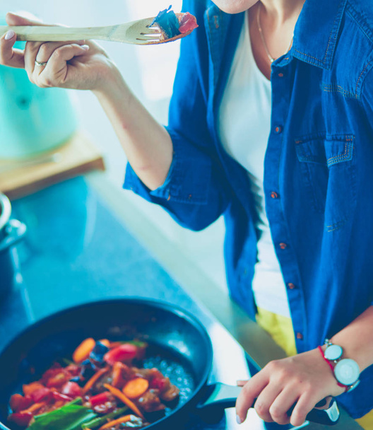 Young woman cooking healthy food holding a pan with vegetables is it. Healthy lifestyle, cooking at home concept - Foto, imagen