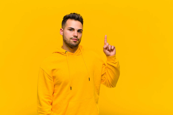young hispanic man feeling like a genius holding finger proudly up in the air after realizing a great idea, saying eureka against orange wall - Fotoğraf, Görsel