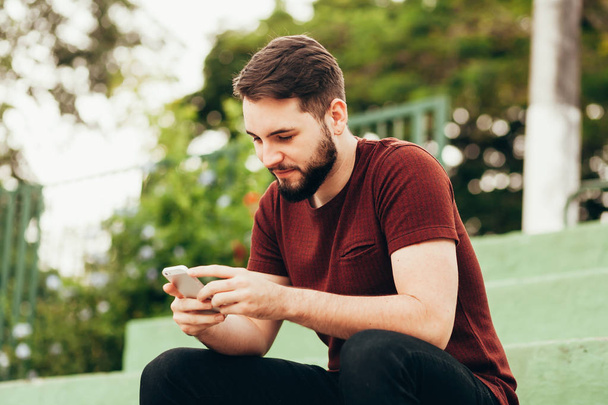 Attractive young smiling man using phone in a public park - Photo, Image