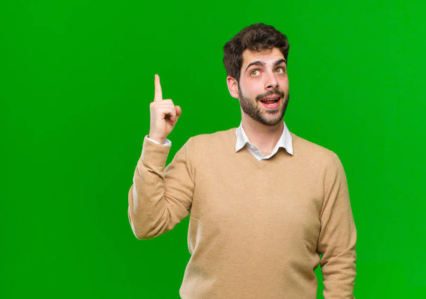 young businessman feeling like a happy and excited genius after realizing an idea, cheerfully raising finger, eureka! against green background - Zdjęcie, obraz