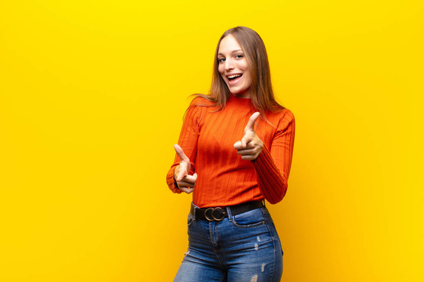 young pretty woman feeling happy, cool, satisfied, relaxed and successful, pointing at camera, choosing you against orange background - Foto, Bild