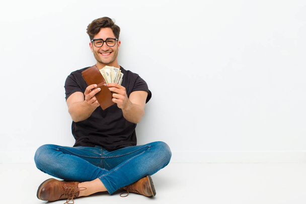 young handsome man with a wallet sitting on the floor sitting on the floor in a white room - Foto, immagini