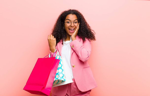 young black pretty woman with shopping bags against pink wall background - 写真・画像