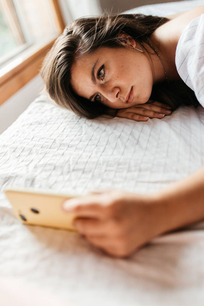 Close up portrait of young sad woman lying on the bed looking at her smartphone feels unhappy. Waiting for mobile message. Feeling worried, hurt, heartbroken lonely ignored, not texting on cellphone - Zdjęcie, obraz