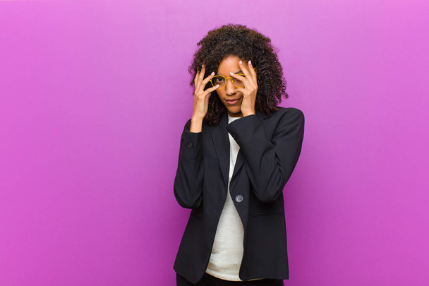 νεαρή μαύρη επιχειρηματίας που νιώθει φοβισμένη ή ντροπιασμένη, κρυφοκοιτάζει ή κατασκοπεύει με τα μάτια μισοσκεπασμένα με τα χέρια - Φωτογραφία, εικόνα