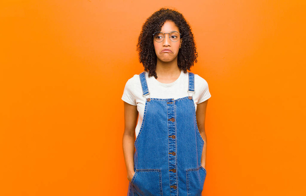young pretty black woman feeling sad and stressed, upset because of a bad surprise, with a negative, anxious look against orange wall - Фото, изображение