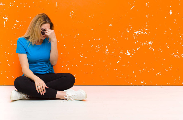 young blonde woman feeling stressed, unhappy and frustrated, touching forehead and suffering migraine of severe headache sitting on the floor - 写真・画像
