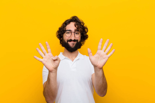young crazy man smiling and looking friendly, showing number nine or ninth with hand forward, counting down against yellow wall - Foto, Bild
