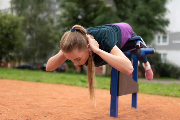 Kaunis urheilullinen tyttö kouluttaa vatsan lihaksia kadulla simulaattori
.  - Valokuva, kuva
