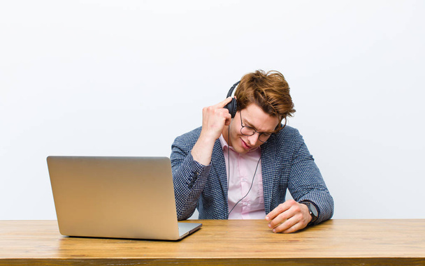 joven hombre de negocios cabeza roja trabajando en su escritorio con auriculares
 - Foto, Imagen
