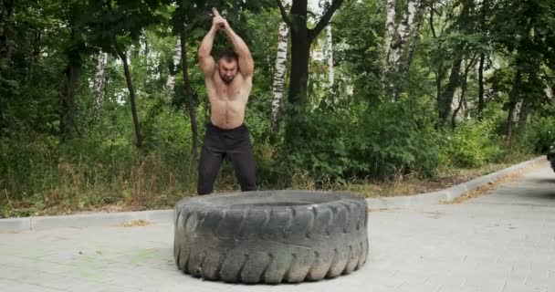 Muscle athlete strongman man hits a hammer on a huge wheel. Slow motion - Footage, Video
