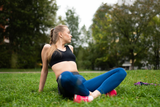 Красивая спортивная девушка в теме, сидящая на траве в расслабленной позе лотоса
. - Фото, изображение