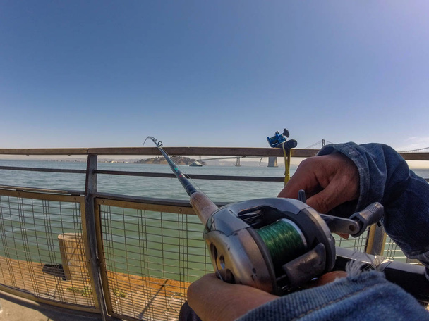 Close-up de mãos humanas segurando uma vara de pesca em primeiro plano, visão fisheye. Conceito, pesca, hobby
. - Foto, Imagem