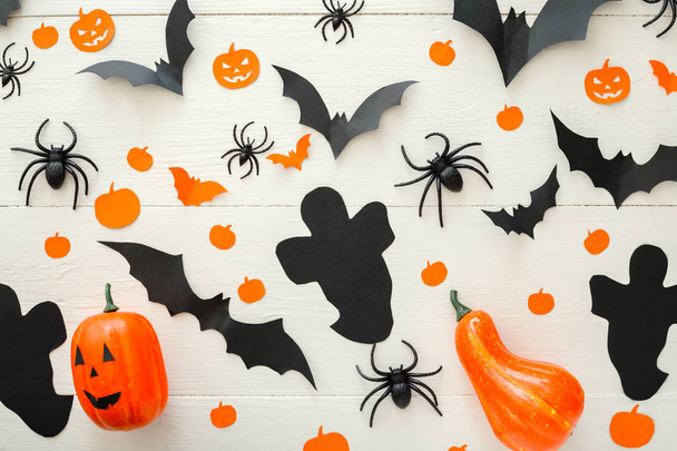 Halloween background with jack-o'-lanter, pumpkins, paper bats, spiders, confetti on white wooden background. Halloween holiday decorations. Flat lay, top view. Party invitation mockup, celebration. - Photo, image