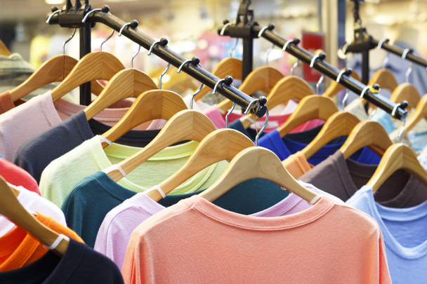 Camisetas multicoloridas em cabides de madeira na loja, vista frontal
. - Foto, Imagem