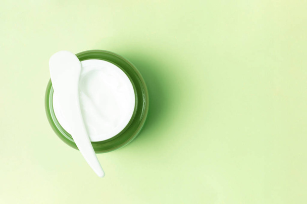 Pot vert avec crème blanche et spatule en plastique sur fond, vue du dessus, espace de copie
 - Photo, image
