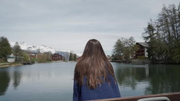 Brunette long-hair girl sitting and looking at a beautiful mountain landscape in front of her. Rear view - Imágenes, Vídeo